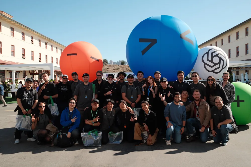 Community members posing together beside colorful inflatable sculptures and an OpenAI logo